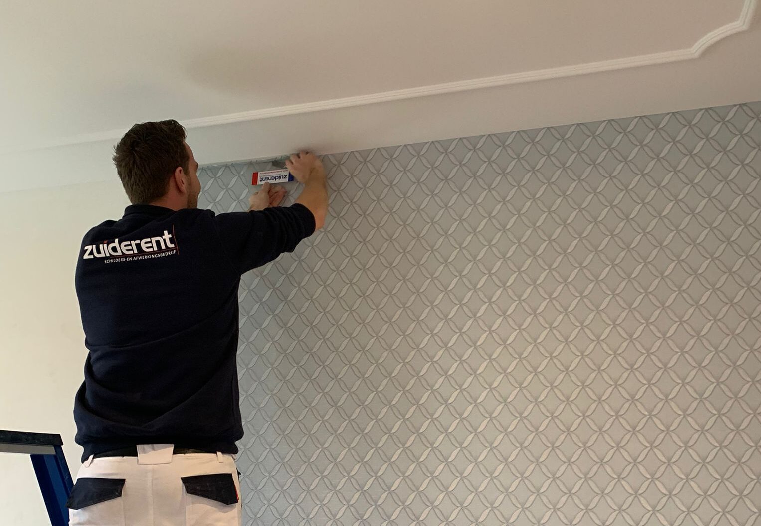 Schilder brengt nauwkeurig behang of wandafwerking aan in een modern interieur, perfect strak en professioneel uitgevoerd.