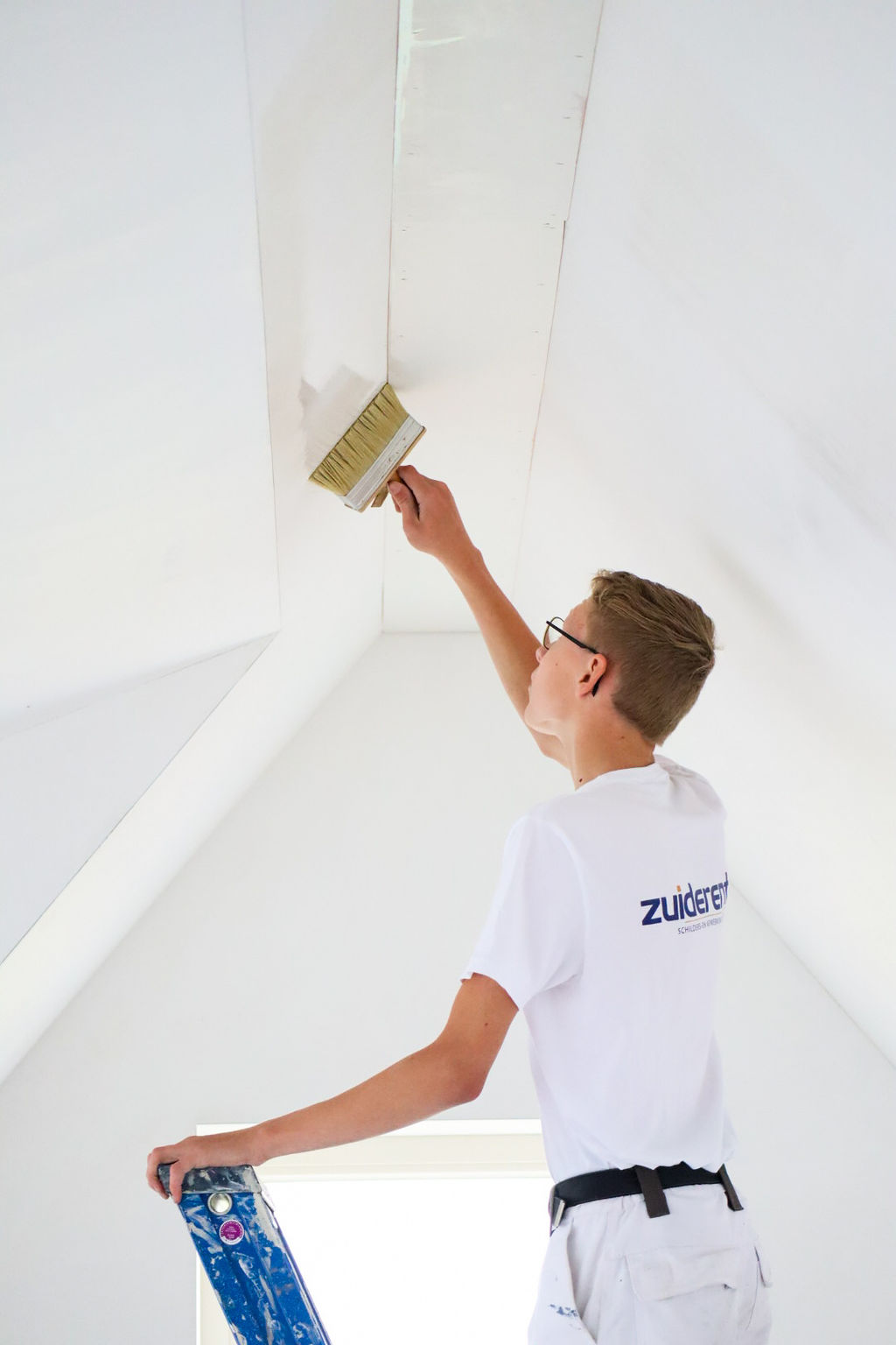 Schilder werkt met een brede kwast aan het witten van een schuin zolderplafond