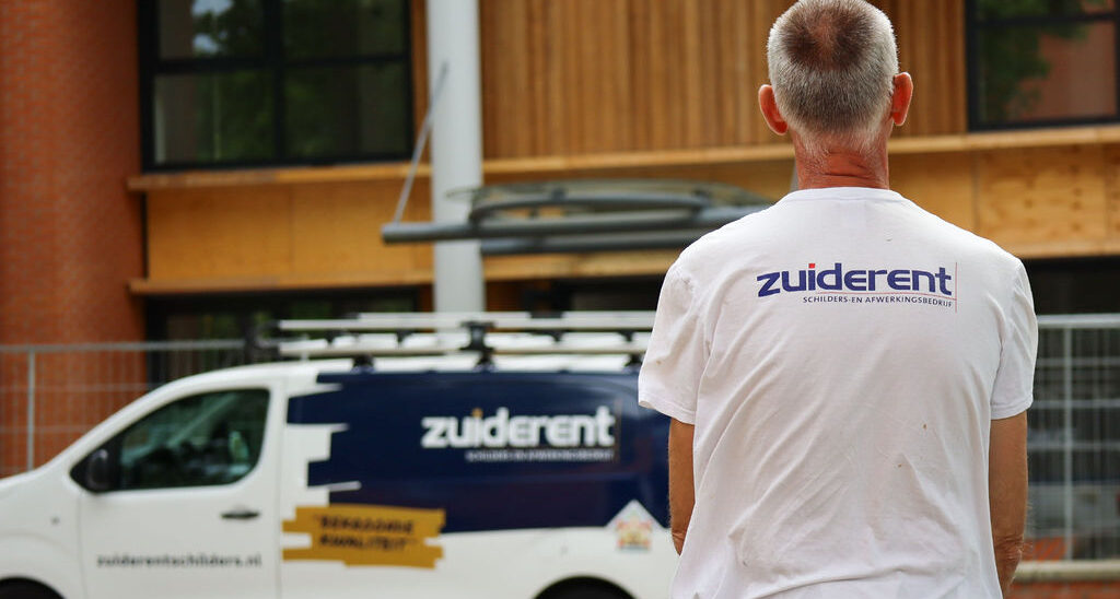 Werknemer van Zuiderent staat met zijn rug naar ons toe in zijn werkkleding met de werkbus op de achtergrond.