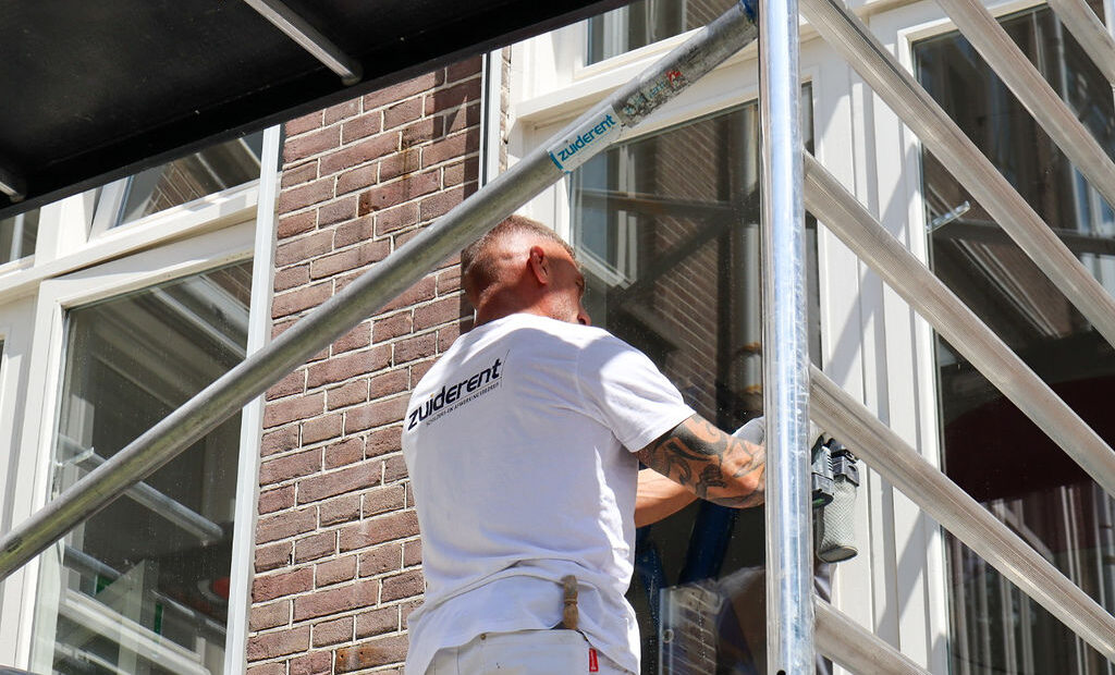 Schilder van Zuiderent werkt op een steiger aan een houten kozijn.